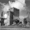 View of three crenelated towers and walls of Guimarães castle, on a slight elevation with trees in the foreground.